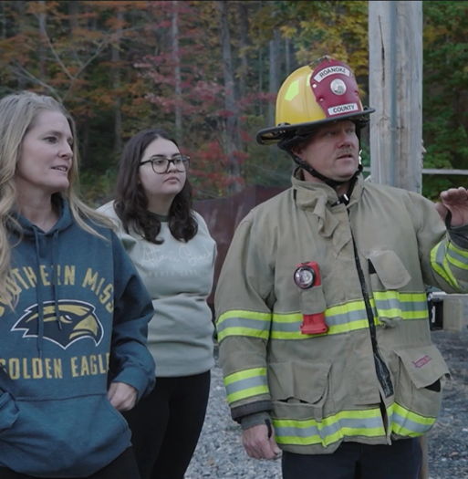 Two people stand with a fire fighter
